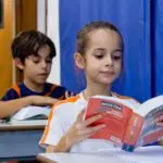 Duas crianças do 3º Ano do Ensino Fundamental, com idade entre 8 e 9 anos, leem atentamente seus dicionários da língua portuguesa em sala de aula.