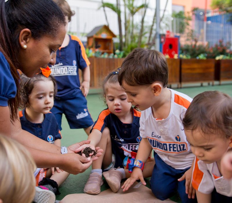 Grupo de crianças da nossa escola infantil olhando para a terra, junto com uma professora